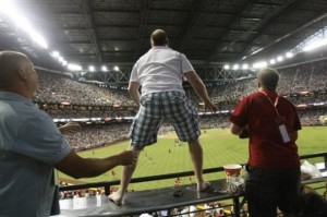 Fan stands barefoot on table to catch ball.